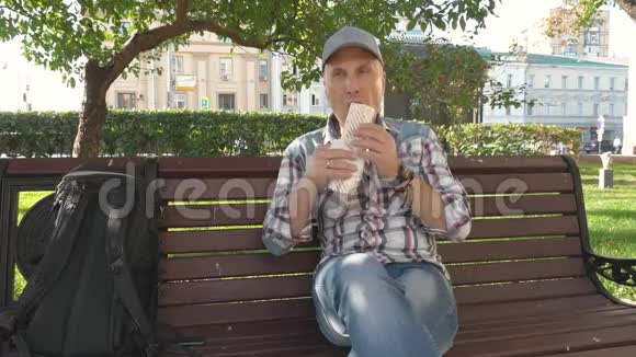 白种人坐在长椅上公园里的中年男子帽吃大三明治视频的预览图
