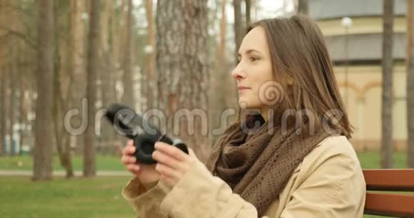 迷人的女人戴上耳机打开音乐同时坐在秋天公园的长凳上欣赏最喜欢的歌曲音乐概念视频的预览图
