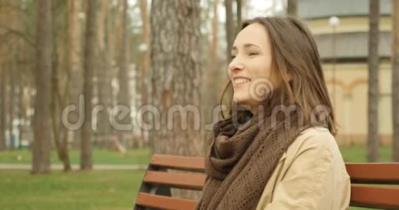 可爱的女孩与相机交谈微笑着坐在秋天公园的长凳上开始打电话视频的预览图