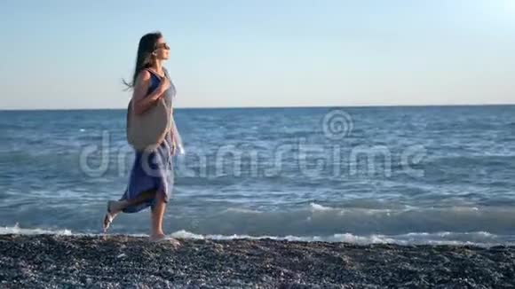可爱优雅的年轻女性穿着裙子在日落海滩的卵石上漫步全程跟踪拍摄视频的预览图