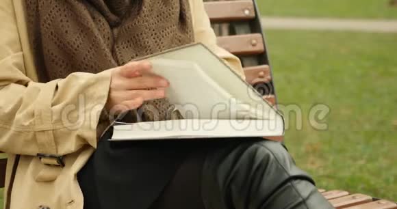 女人一边打开书一边翻页读书的概念带棕色围巾的女人在公园看书视频的预览图