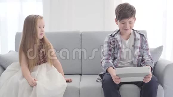 白种人小男孩看着平板电脑屏幕的肖像可爱的女孩坐在他旁边害羞地瞥了一眼她的爱视频的预览图
