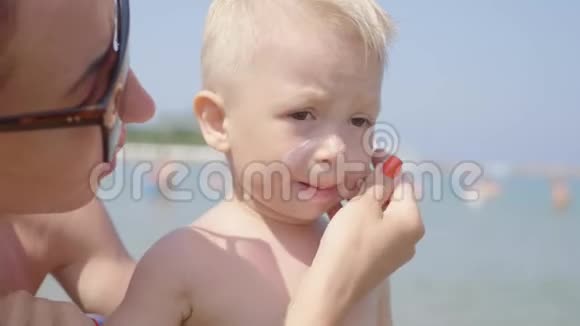 妈妈在暑假期间给可爱的幼儿男孩涂防晒霜儿童保健视频的预览图