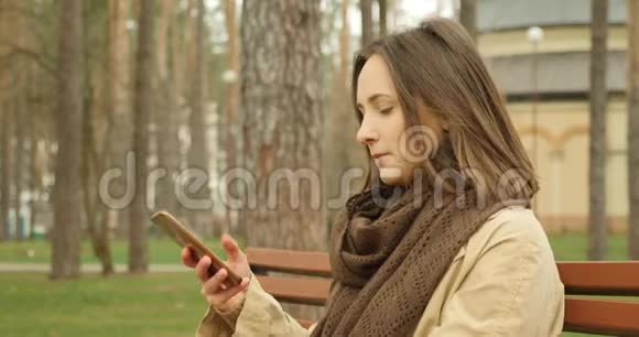 迷人的女孩开始在电话上交谈笑着在秋天公园的长凳上交谈视频的预览图