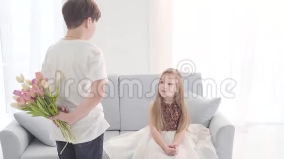 白人男孩把郁金香花束送给坐在沙发上的迷人女孩小姑娘送礼物闻花香视频的预览图