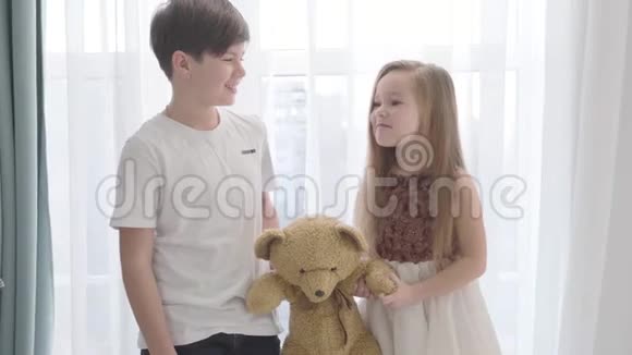 小白种人女孩和男孩抱着泰迪熊互相看着微笑着快乐的孩子花时间视频的预览图