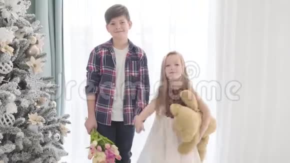 白人男孩和女孩站在圣诞树旁边握手的肖像布鲁内特男孩视频的预览图