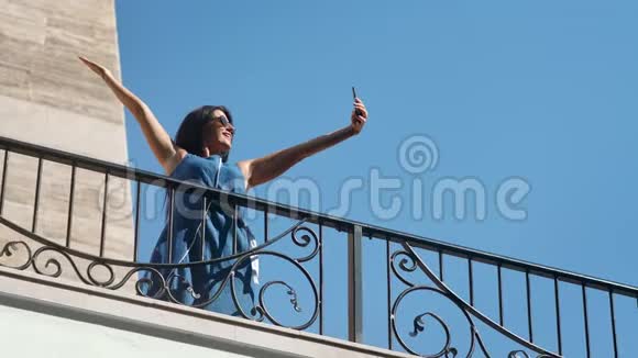 快乐的游客深色头发的女性玩着玩用智能手机在阳台上自拍视频的预览图