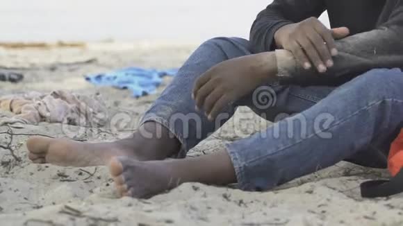 沮丧的非裔美国男性难民独自坐在居民岛海滩上视频的预览图