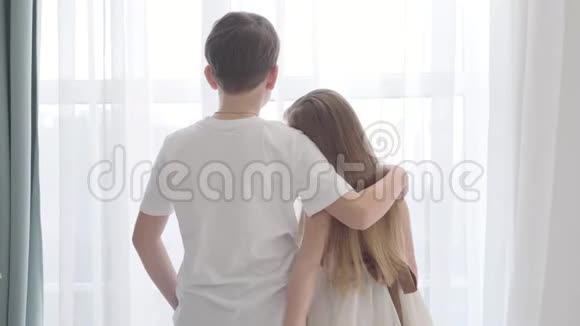 镜头接近白种人女孩和男孩站在窗前孩子们拥抱着看着视频的预览图