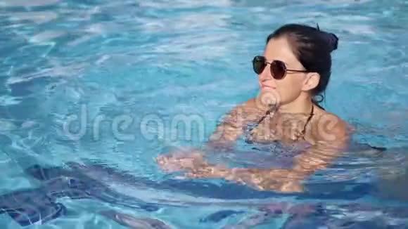 戴着太阳镜的快乐女人在游泳池里放松享受暑假视频的预览图