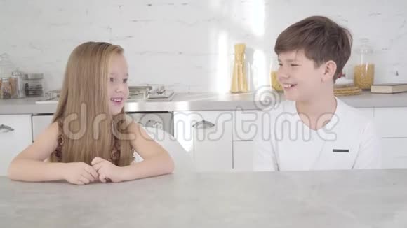两个白种人的孩子坐在桌子旁互相看着对方做着安静的手势开朗的男孩和女孩视频的预览图