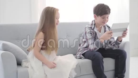 小可爱的白种人女孩靠近男孩在平板电脑屏幕上看电影穿裙子的害羞女孩等待关注视频的预览图