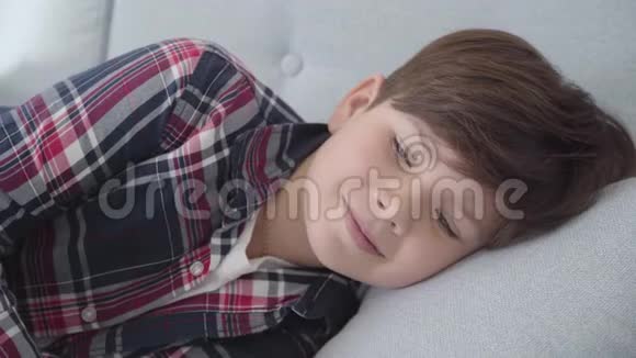 可爱的白人男孩的特写肖像棕色头发和灰色的眼睛躺在柔软的枕头上微笑的孩子躺在视频的预览图