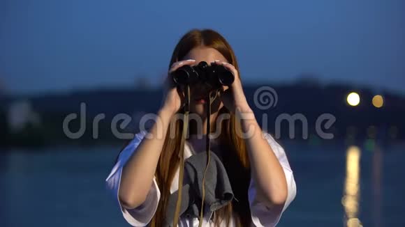 好奇的女孩晚上在河堤上用望远镜看视频的预览图