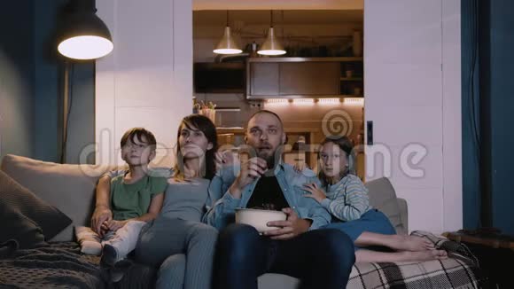 快乐微笑的年轻白种人母亲父亲和两个孩子一起在家里的沙发上看电影使用在线电影视频的预览图