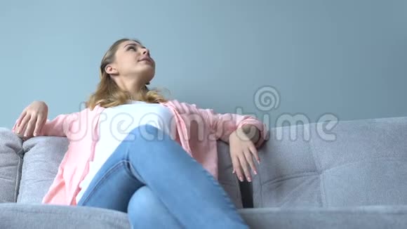 漂亮的年轻女士坐在沙发上放松对装修感到满意视频的预览图