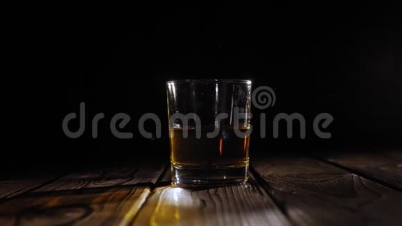 在木制背景上一堆冰块掉进一杯威士忌里视频的预览图
