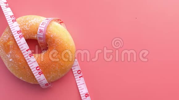 在粉红色背景上关闭测量磁带和甜甜圈视频的预览图