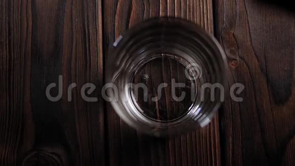 在一个空杯子里倒威士忌或白兰地在一个黑暗的木制表面顶部视图视频的预览图