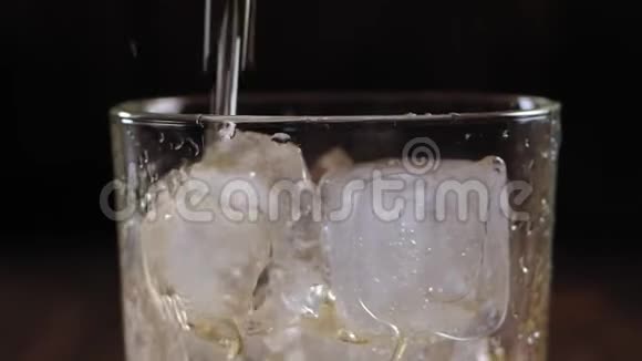 在棕色的木制背景下将威士忌倒入装有冰块的玻璃杯中视频的预览图