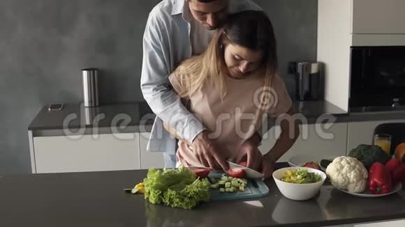 可爱的一对在灰色厨房一起做饭年轻女子和丈夫一起切蔬菜高个子男人视频的预览图