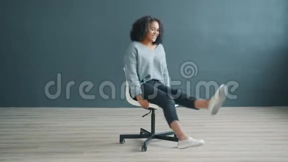 戏谑的非裔美国女孩在灰色背景的办公椅上旋转的肖像视频的预览图
