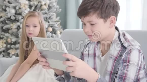 侧面看快乐的白人男孩坐在平板电脑和微笑漂亮的女孩看着他的背景害羞可爱视频的预览图