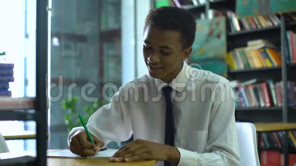 勤奋的非裔美国男学生在笔记本上做作业在摄像机上微笑视频的预览图