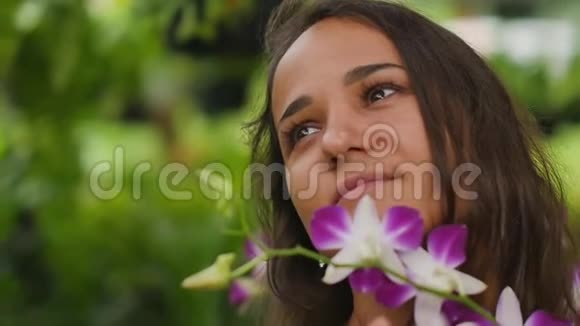 在花园里微笑着美丽的年轻女子一个女人摸着兰花享受它的气味慢动作视频的预览图