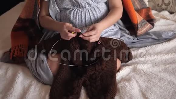 一位孕妇为她的孩子编织一件温暖的衣服坐在床上特写视频的预览图
