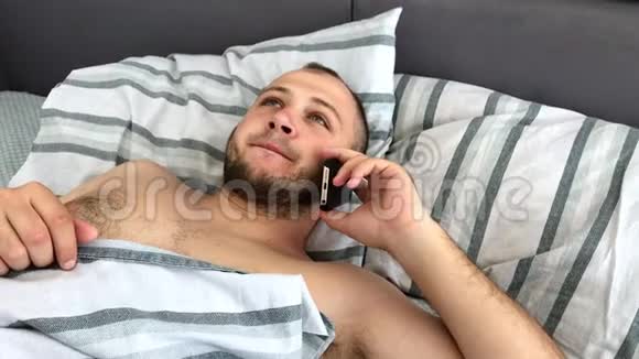 一个年轻人躺在床上用智能手机说话或打电话俯视图视频的预览图