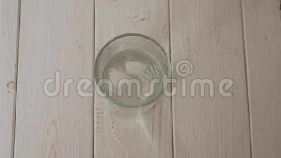 一个冰落在一个轻木表面的一整杯水的特写视频的预览图