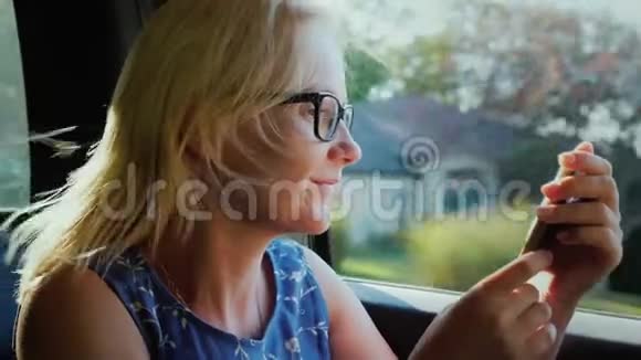 一个女人坐在乘客座位上的汽车里旅行在路上使用智能手机窗外是典型的视频的预览图