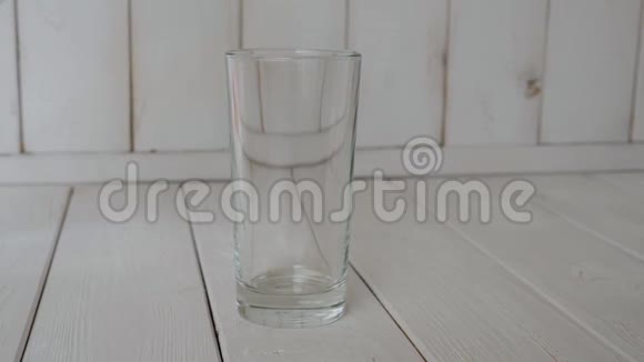 特写干净的水倒在一个玻璃上的浅色木制背景视频的预览图