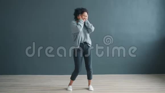 快乐的非裔美国女士戴着无线耳机在灰色背景下跳舞视频的预览图