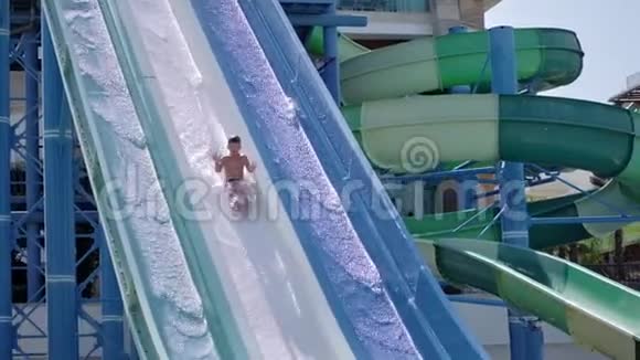 快乐活跃晒黑的男孩在水上乐园滑水积极慢动作视频的预览图
