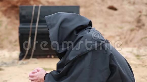一个穿着黑袍带着头巾的和尚坐在空地上在炉火旁取暖视频的预览图