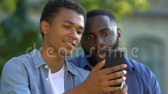 非洲裔美国青少年在智能手机上向微笑的男人家人展示照片视频的预览图