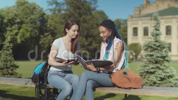 两个快乐的女学生坐在长凳上聊天视频的预览图