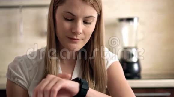 坐在厨房里的漂亮年轻女子在室内通过她的智能手表发送语音信息视频的预览图
