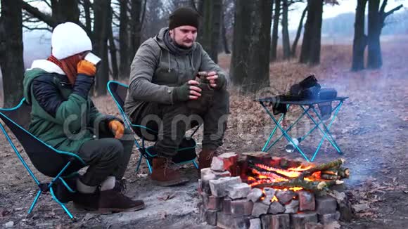 有几个人坐在炉火旁的光椅上寒冷的秋晚在森林里积极的生活方式旅行度假视频的预览图