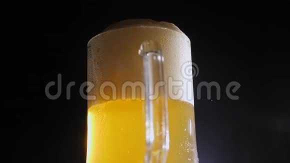 一杯带有泡沫的淡啤酒慢慢地在黑色背景上旋转特写镜头视频的预览图