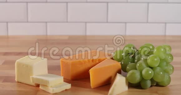 手把块奶酪和面包片放在奶酪小吃托盘上然后从茎上摘一颗绿色葡萄视频的预览图