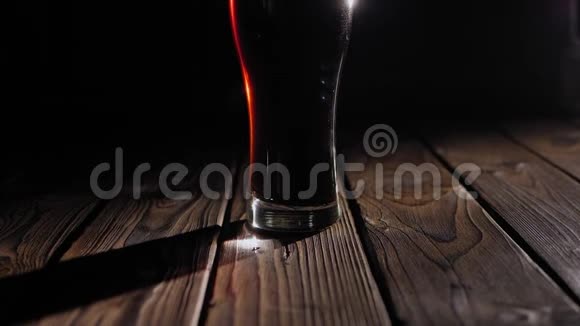 在黑色背景上的木制表面上特写一杯冰镇深色啤酒视频的预览图