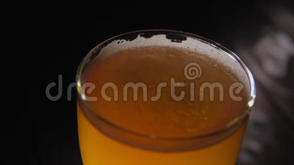 在黑暗中在木制背景上用泡沫旋转的啤酒杯特写视频的预览图