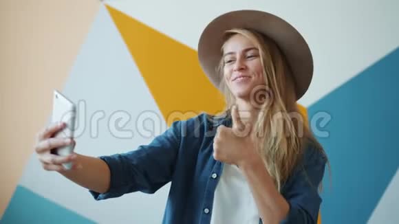 漂亮的年轻女士戴着帽子用智能手机拍照自拍视频的预览图