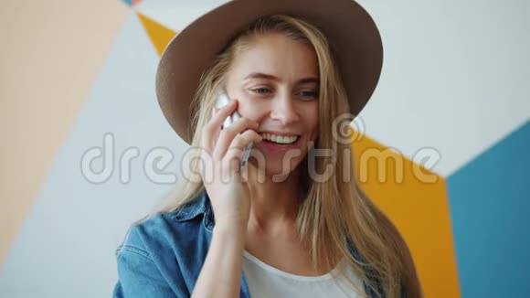 戴着帽子的漂亮年轻女士在手机上笑着说话视频的预览图