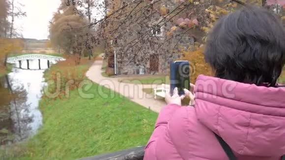 多云秋日白桥池塘女人在智能手机上拍自然照片视频的预览图