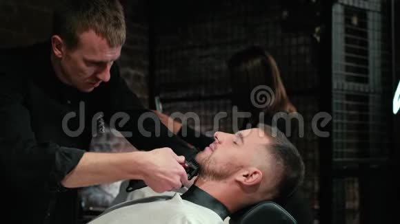 巴伯把客户的胡子剃在椅子上胡子的发型用电动剃须刀刮胡子装饰视频的预览图